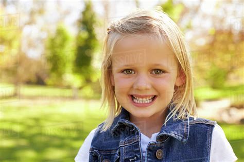Five Year Old Blonde Girl In A Park Smiling To Camera Stock Photo
