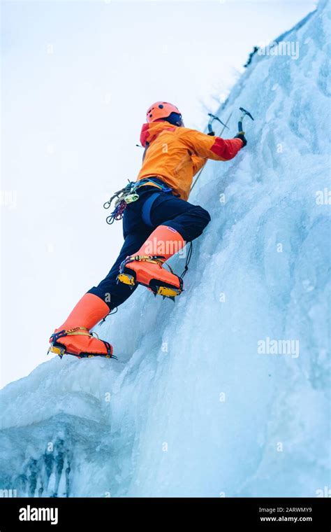 Low Angle Shot Of An Ice Climber In Orange Suit Climbing An Icy