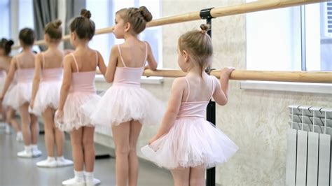 Rear View Of Group Of Little Girls Using Ballet Barre When Doing Leg