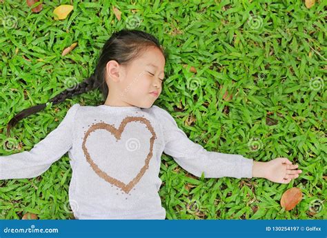 Happy Cute Little Asian Child Girl Lying On Green Lawn Smiling And