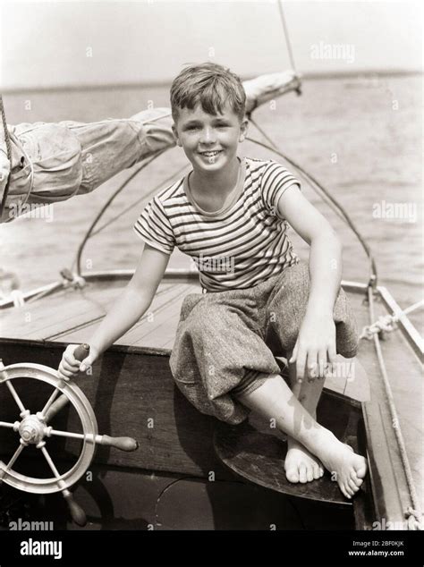 1930s Smiling Towheaded Enthusiastic Barefooted Boy Sitting At The