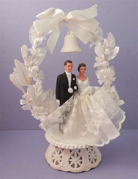 A Wedding Cake Topper With A Bride And Groom Under A Bell On The Table