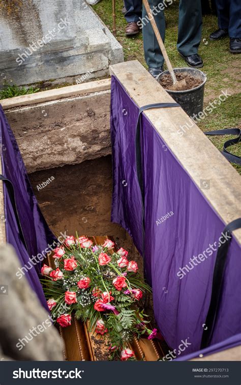 Mourners Staying By The Opened Grave Burying A Coffin At A Cemetery
