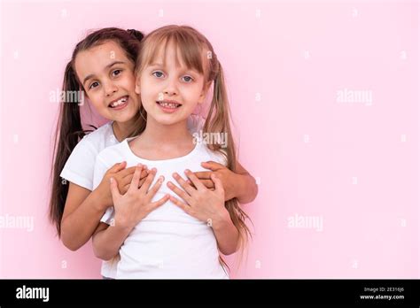 Two Little Girls Hugging Each Other Isolated On On A Pink Background