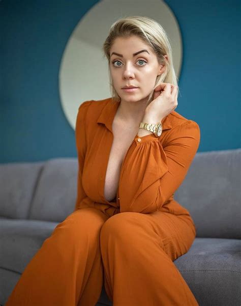 A Woman In An Orange Jumpsuit Sitting On A Gray Couch With Her Hand