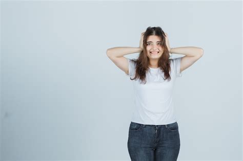Молодая девушка держит руки на голове в футболке джинсах и выглядит смущенным вид спереди