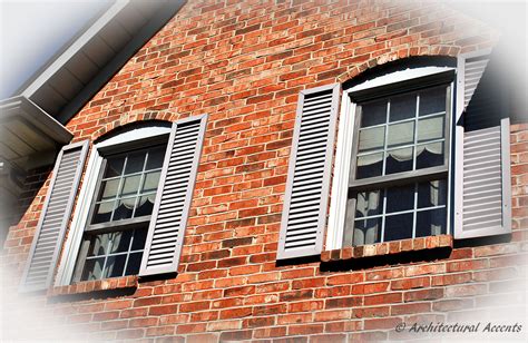 Two Windows On The Side Of A Brick Building With White Shutters And