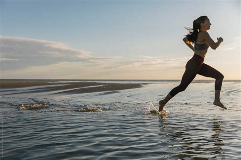 Beautiful Fit Female Athlete Running On Beach Through Water By