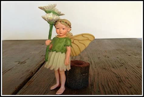 A Fairy Figurine Holding A Flower On Top Of A Wooden Table