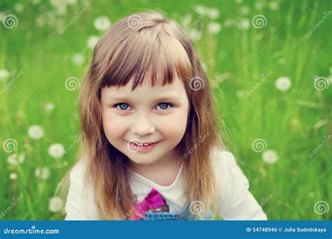 Stående Av Den Gulliga Lilla Flickan Med Härligt Leende Och Blåa ögon Som Sitter På Blommaängen