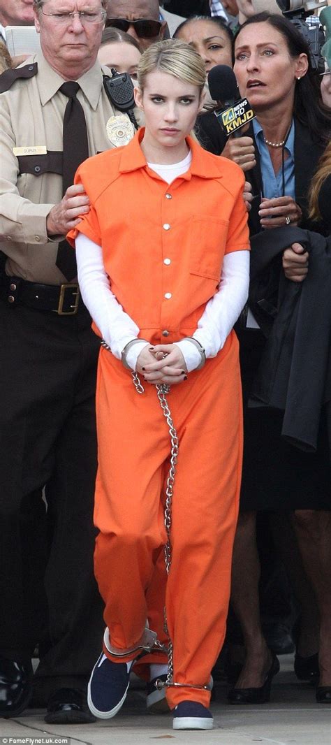 a woman in an orange prison outfit is being escorted by police and surrounded by reporters