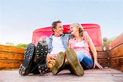 Senior Couple Sitting In Back Of Vintage Red Pickup Truck Hugging