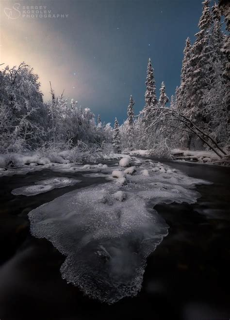 An Icy River Surrounded By Snow Covered Trees Under A Full Moon Filled