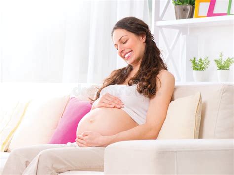 Mujer Sonriente Embarazada Que Se Sienta En Un Sofá Foto de archivo