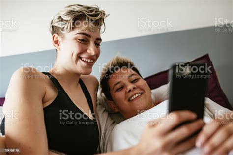 Hispanic Lesbian Couple In Morning In Bed Using Smart Phones Stock
