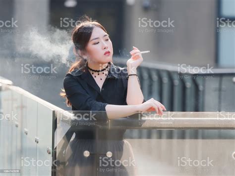 portrait of beautiful chinese girl in black dress smoking a cigarette outdoor in sunny day stock
