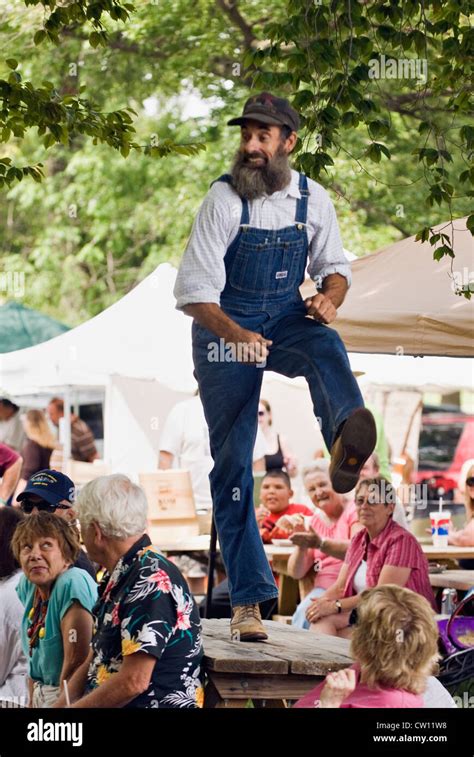 Man In Bib Overalls Dancing A Jig On A Picnic Table Amid Crowd At The