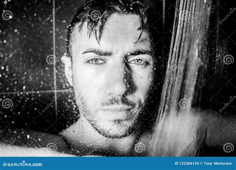 hunky handsome man male with beard and muscular arms is wet in shower looking at camera stock