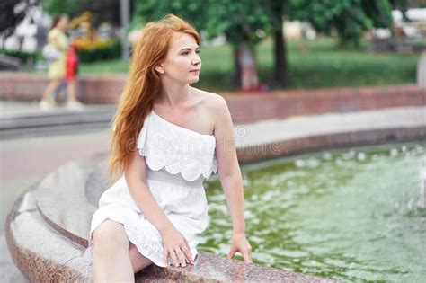 Attractive Redhead Girl Sitting Near The Fountain In The City