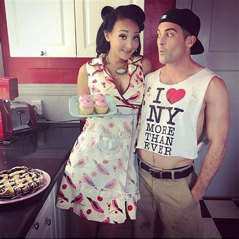A Man And Woman Standing Next To Each Other In Front Of A Table With Cookies On It