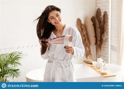 Woman Drying Long Brunette Hair Using Hairdryer In Bathroom Stock Photo