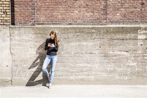 Woman With Leaning Against Wall Using Cell Phone Stock Photo