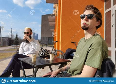 Two Young Hipster Guy Sitting In A Cafe Chatting And Drinking Coffee