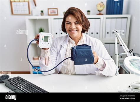 Middle Age Hispanic Doctor Woman Using Blood Pressure Monitor Smiling