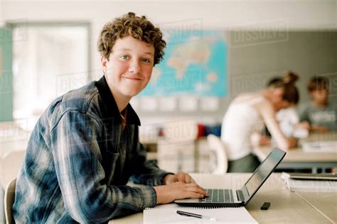 Portrait of teenage boy using laptop while sitting in classroom - Stock Photo - Dissolve