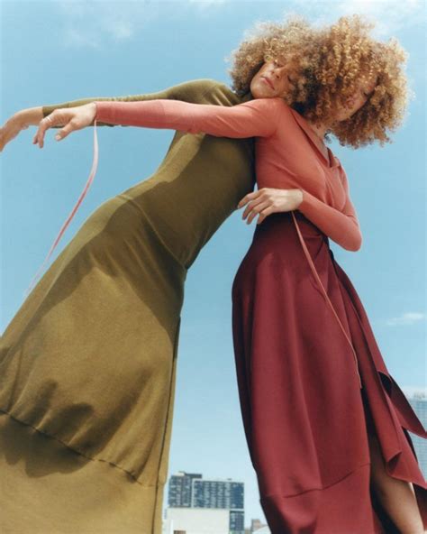 Two Women In Long Dresses Are Dancing On The Beach With Their Arms