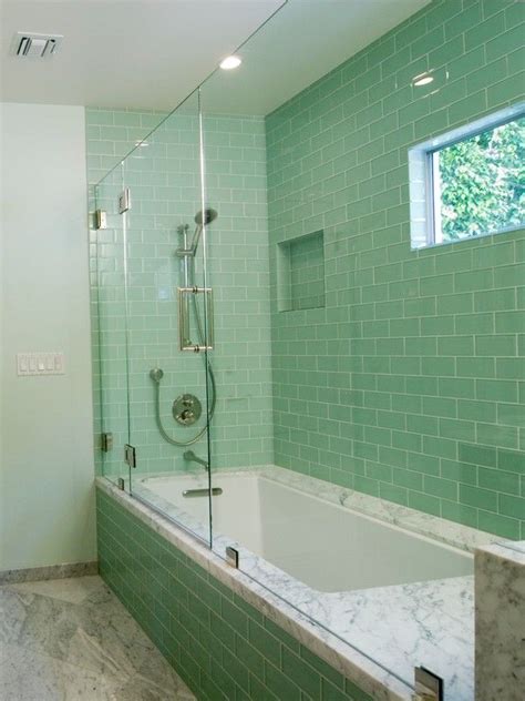 A Bath Tub Sitting Next To A Window In A Bathroom With Green Tiles On