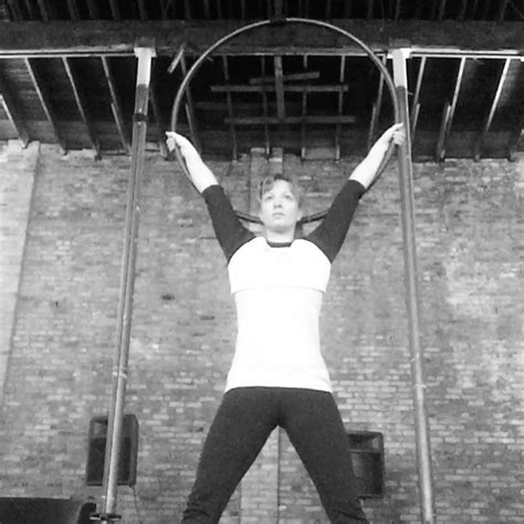 a woman standing on top of a metal bar in front of a brick wall holding onto two large bars