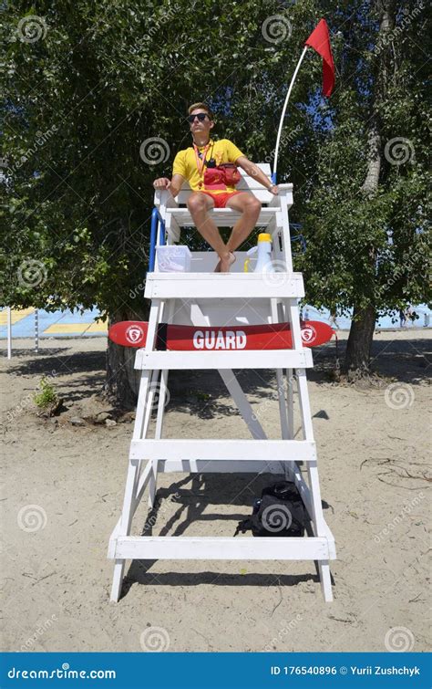 man lifeguard sitting on the chair under the sun umbrella near the swimming pool editorial image