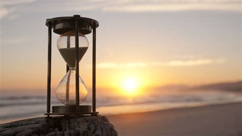 An Hourglass Sitting On Top Of A Rock Next To The Ocean At Sunset Or Sunrise