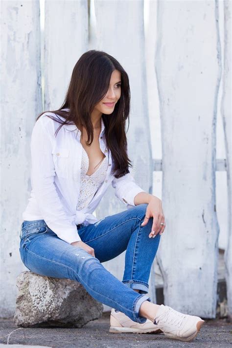 mooi glimlachend meisje leeg wit overhemd dragen en jeans die tegen straat houten muur stellen