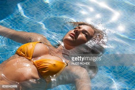 Beautiful Young Woman Floating In Sunlit Swimming Pool Wearing Yellow