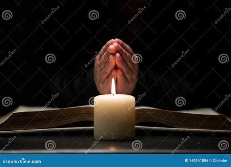 Person Praying With Hands Over Bible Illuminated By Candle Light Stock