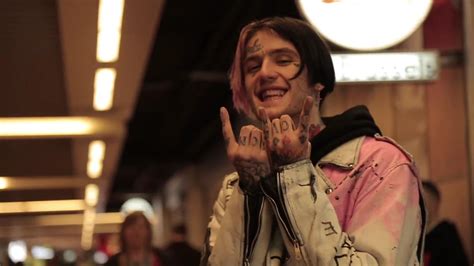 Smiley Lil Peep Is Showing Hand Signs In Blur Light Background Wearing