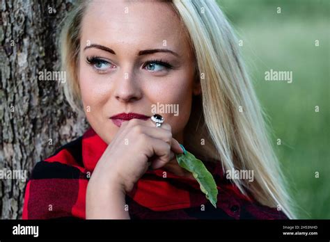 Young Blond Woman Looks To The Left While Leaning Against A Tree She