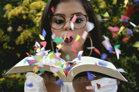 A Woman Wearing Glasses Reading A Book Surrounded By Confetti And
