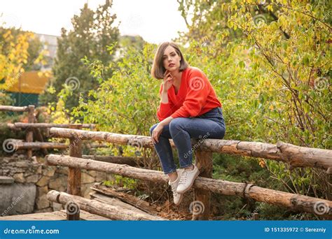 Beautiful Fashionable Woman Sitting On Wooden Fence Outdoors Stock