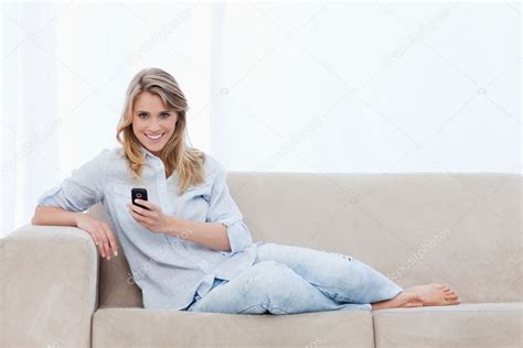 A Woman Sitting On A Couch Holding A Mobile Phone Is Smiling Stock Photo Wavebreakmedia