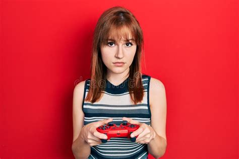 Redhead Young Woman Playing Video Game Holding Controller Relaxed With Serious Expression On