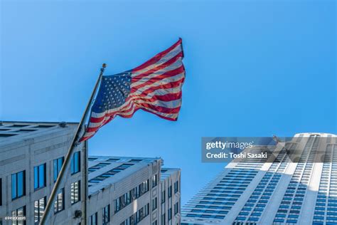 The American National Flag Is Swaying By Wind Among The Building At