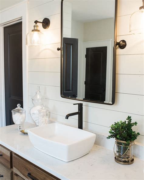 Black and white master bathroom features black vanity mirrors hung from a vertical shiplap wall over a black dual washstand donning matte black hardware and a white and gray marble countertop finished with matte black faucets. Reece Homes on Instagram: "The black framed pivot mirrors ...