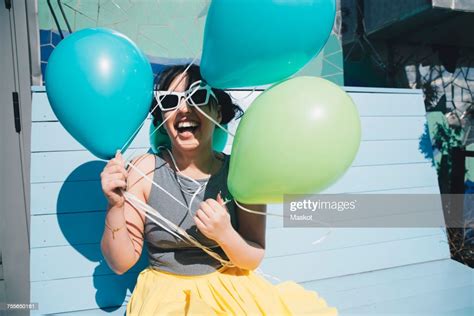 Happy Young Woman Holding Balloons While Sitting On Bench Photo Getty