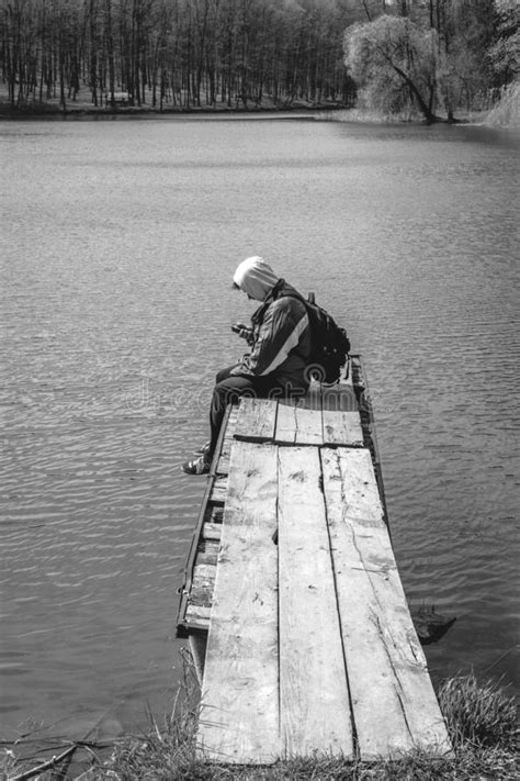 A Sad Man Is Sitting Alone On Pier By The Lake Forest Black And White