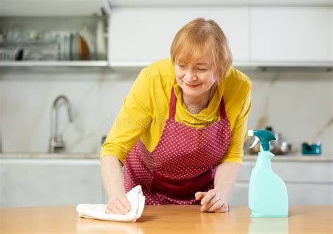 Mature Woman In An Apron Cleaning The Kitchen With Cleaning Products