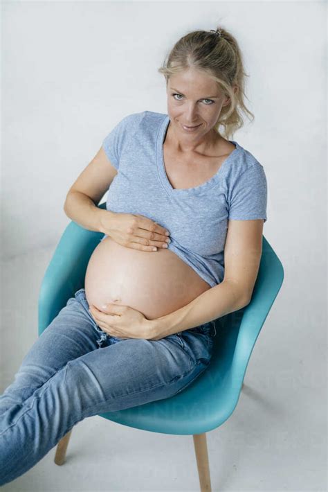 Portrait Of Smiling Pregnant Woman Sitting On A Chair Showing Her Belly