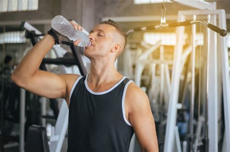 Attractive Strong Man Standing And Drinking Water In Gymmale Break And